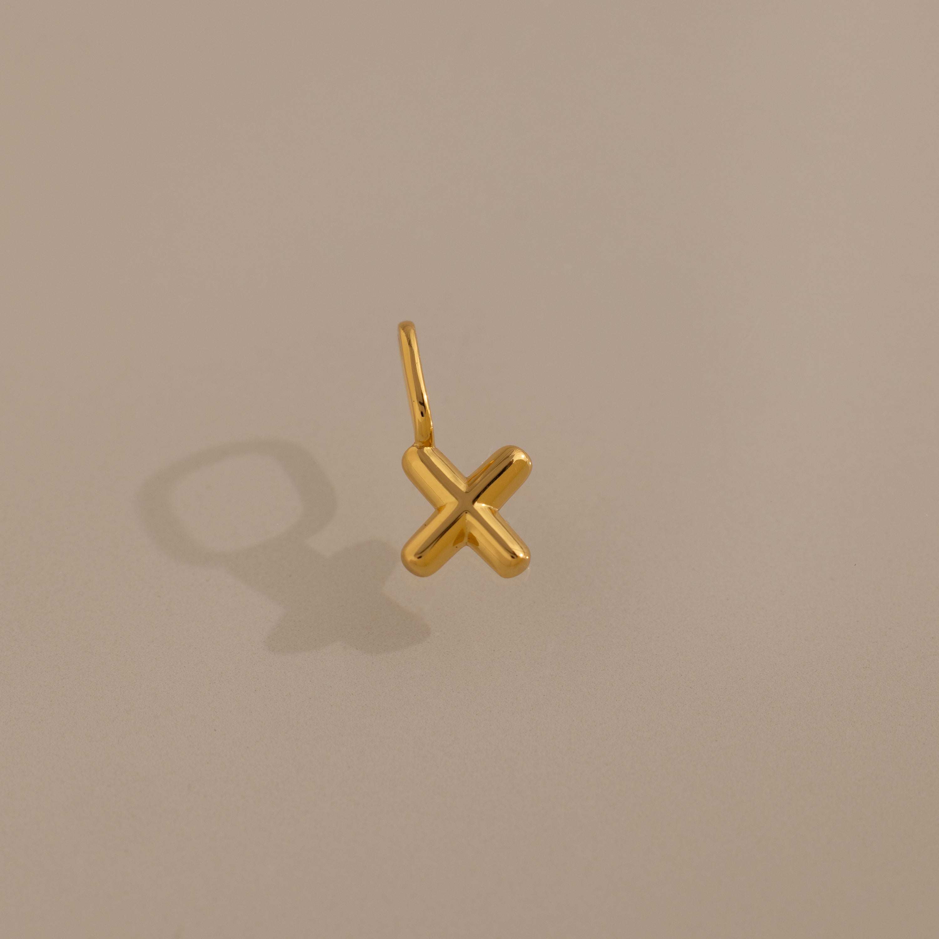 The Bubble Letter Charm in 18K Gold rests on a beige background, casting a shadow left—ideal for personalized jewelry or as a unique addition to any bracelet collection.