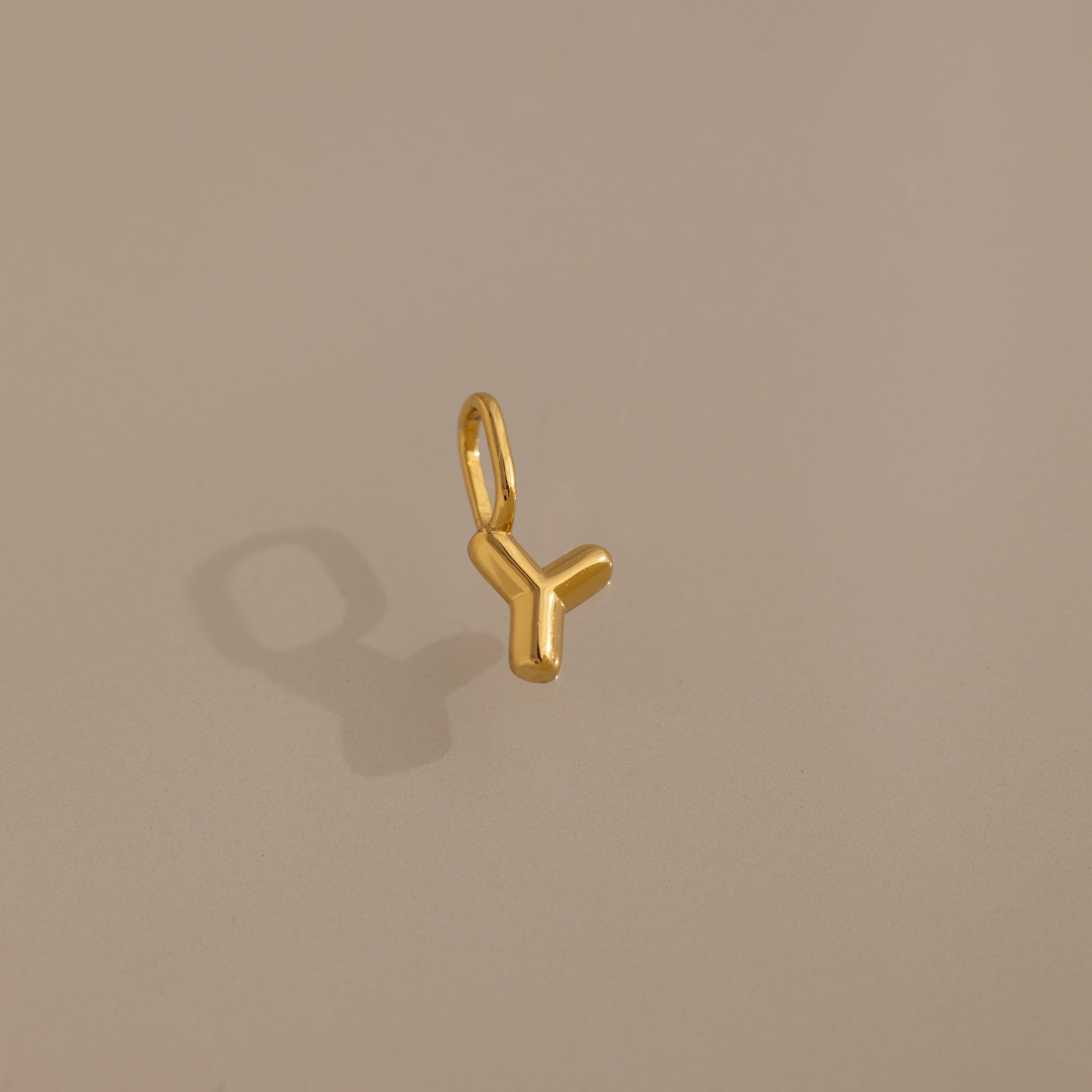 The Bubble Letter Charm in 18K Gold, shaped like the letter Y, is displayed on a beige background with a soft shadow—ideal as a personalized jewelry charm for bracelets.