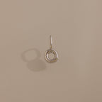 The Bubble Letter Charm in Sterling Silver, a small circular pendant, casts a shadow on a beige surface.