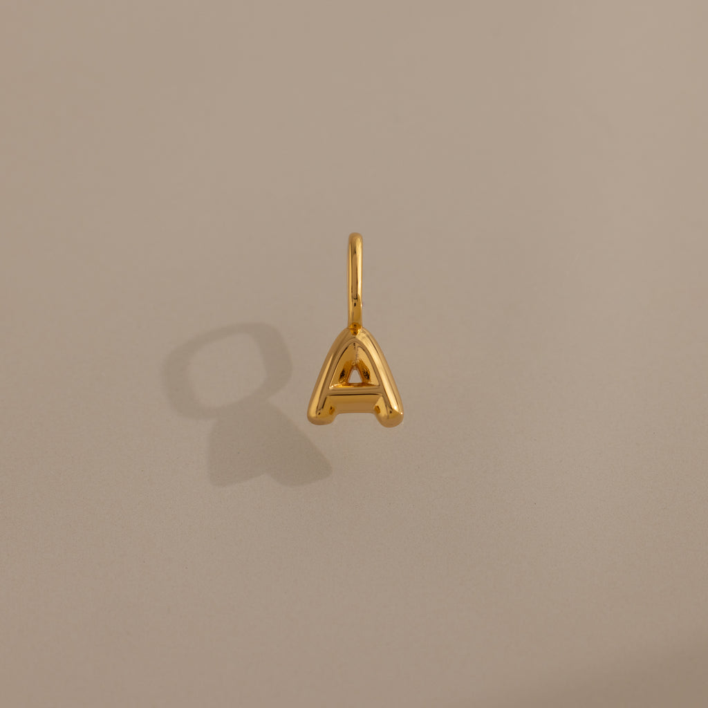 Bubble Letter Charm in 18K Gold shaped as an "A" shown on a plain beige background, casting a subtle shadow to the left.