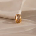 The Bold Pave Dome Charm in 18K Gold features a wide, sparkling band and rests on a soft beige surface—an ideal statement piece for any elegant occasion.