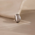The Bold Pave Dome Charm in Silver features rows of sparkling small diamonds on a soft beige fabric background, adding timeless sophistication to any look.
