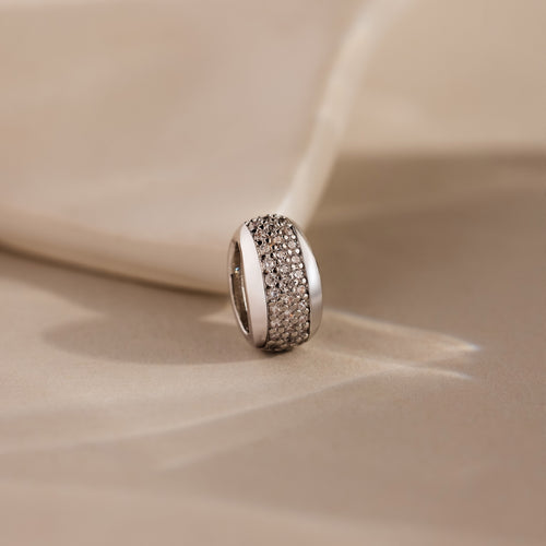 The Bold Pave Dome Charm in Silver features rows of sparkling small diamonds on a soft beige fabric background, adding timeless sophistication to any look.