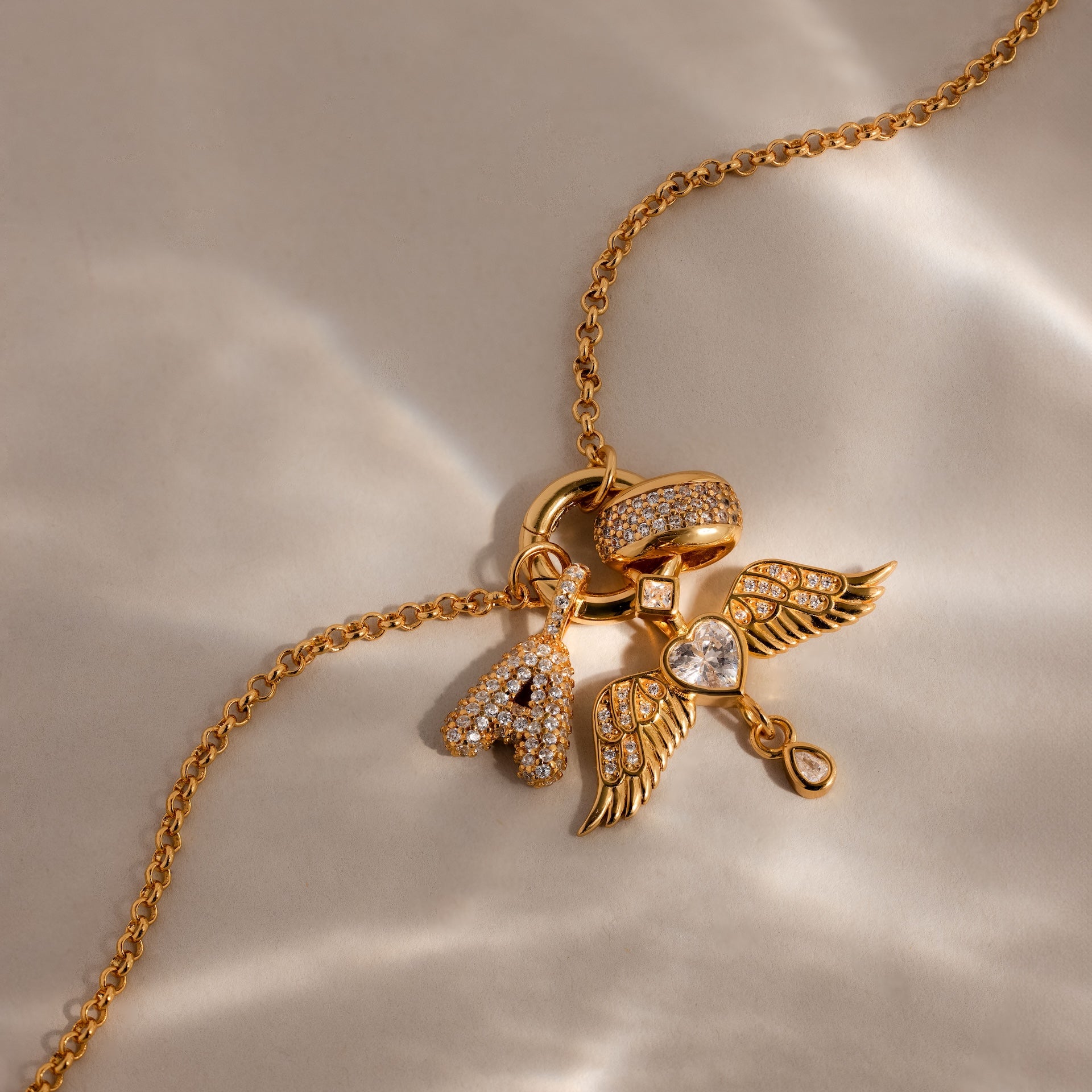 The Bold Pave Dome Charm in 18K Gold features a letter A, wing, heart, and ring—each adorned with sparkling stones. This personalized accessory shines with style and meaning.
