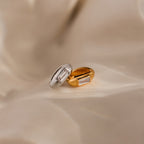 The Baguette Diamond Charm in 18K Gold, featuring a rectangular gemstone, is elegantly displayed on a soft beige fabric background—ideal for those seeking timeless gemstone jewelry.