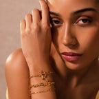 A woman poses gracefully with her hand near her face, drawing attention to the Connector Clasp she wears—an elegant piece that stands out in this exquisite jewelry showcase.