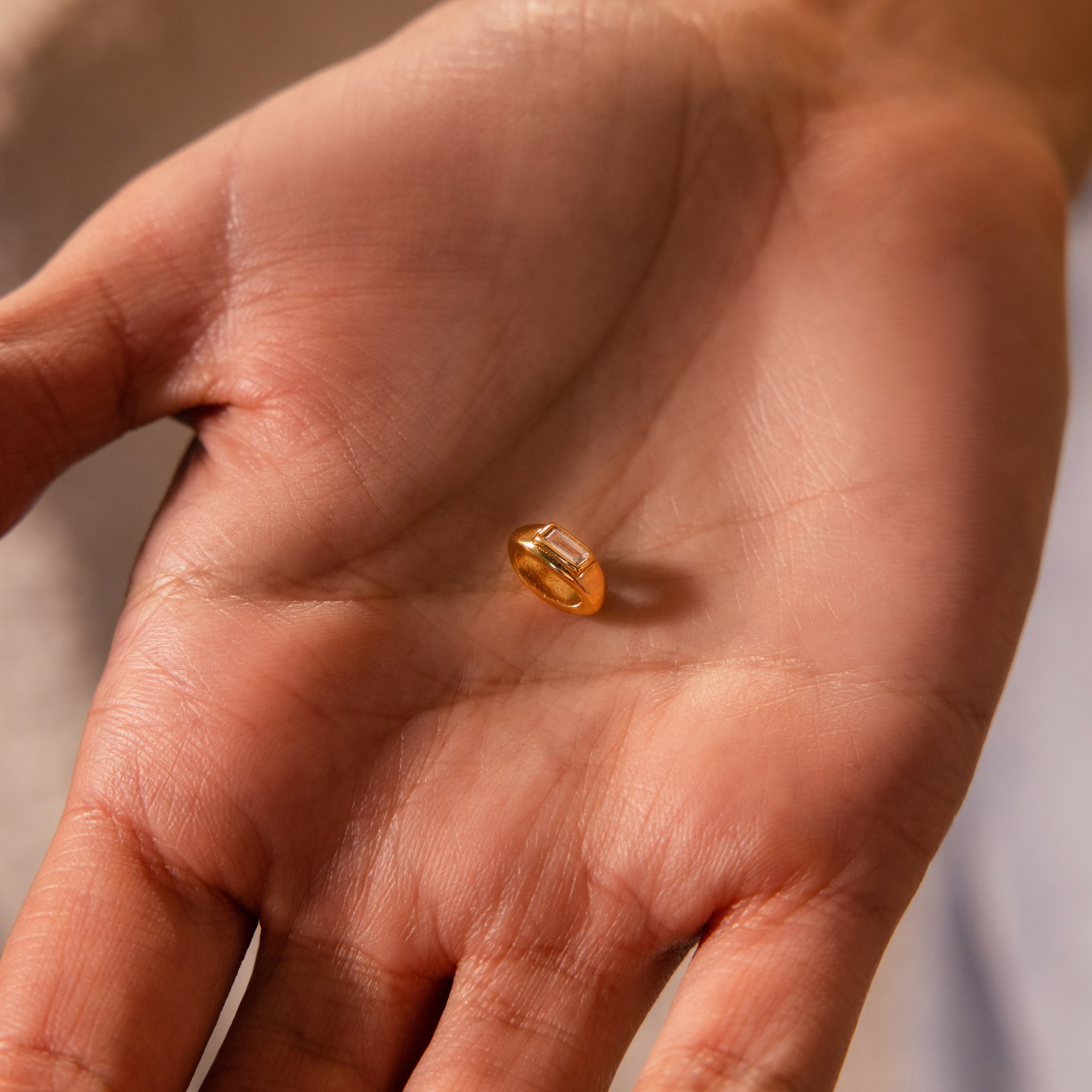 A close-up of a hand holding the Baguette Diamond Charm in 18K Gold.