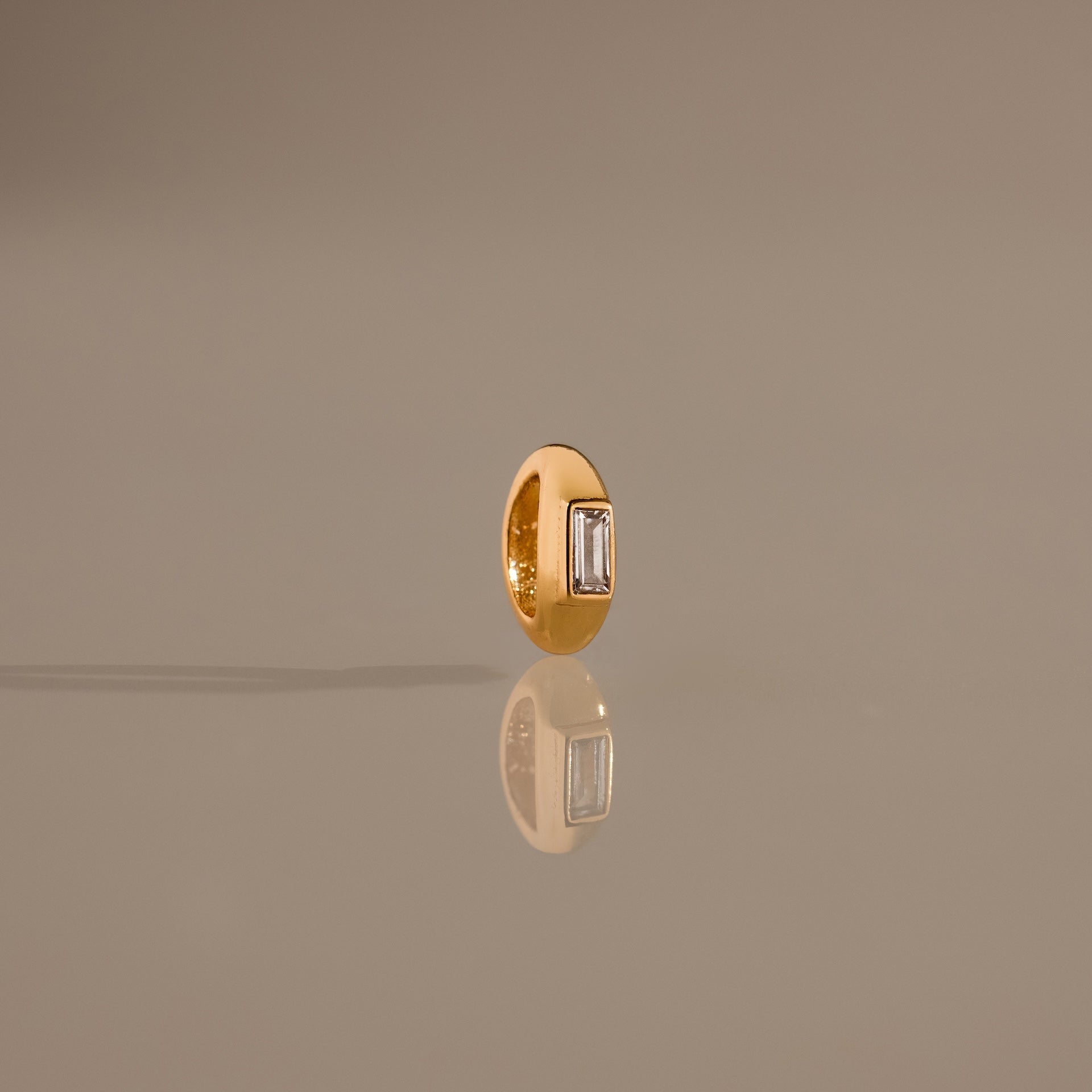 The Baguette Diamond Charm in 18K Gold features a rectangular clear gemstone set upright, reflecting light beautifully for an elegant touch to any jewelry collection.