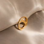 A Connector Clasp in gold with a modern design rests on soft, beige fabric under gentle, diffused lighting.