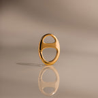The Connector Clasp features a shiny gold oval design with two cutout sections, standing upright on a reflective surface for a modern, elegant look—ideal for adding a touch of luxury to your décor.