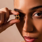 A woman holds the Connector Clasp close to her eye, gazing through it with a soft, focused expression—showcasing the timeless elegance of this stunning accessory.