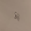 The Knot Charm Clasp in Silver, expertly photographed on a plain beige background, is a small metal clasp with a loop, perfect for jewelry making or crafts.