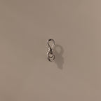 The Knot Charm Clasp in Silver, expertly photographed on a plain beige background, is a small metal clasp with a loop, perfect for jewelry making or crafts.