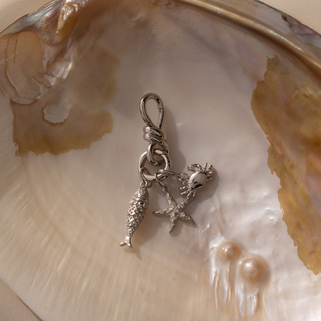 Knot Charm Clasp in Silver: Elegant keychain featuring fish, starfish, and seashell charms, artfully displayed on an iridescent oyster shell with two pearls. Perfect ocean-inspired accessory for any occasion.