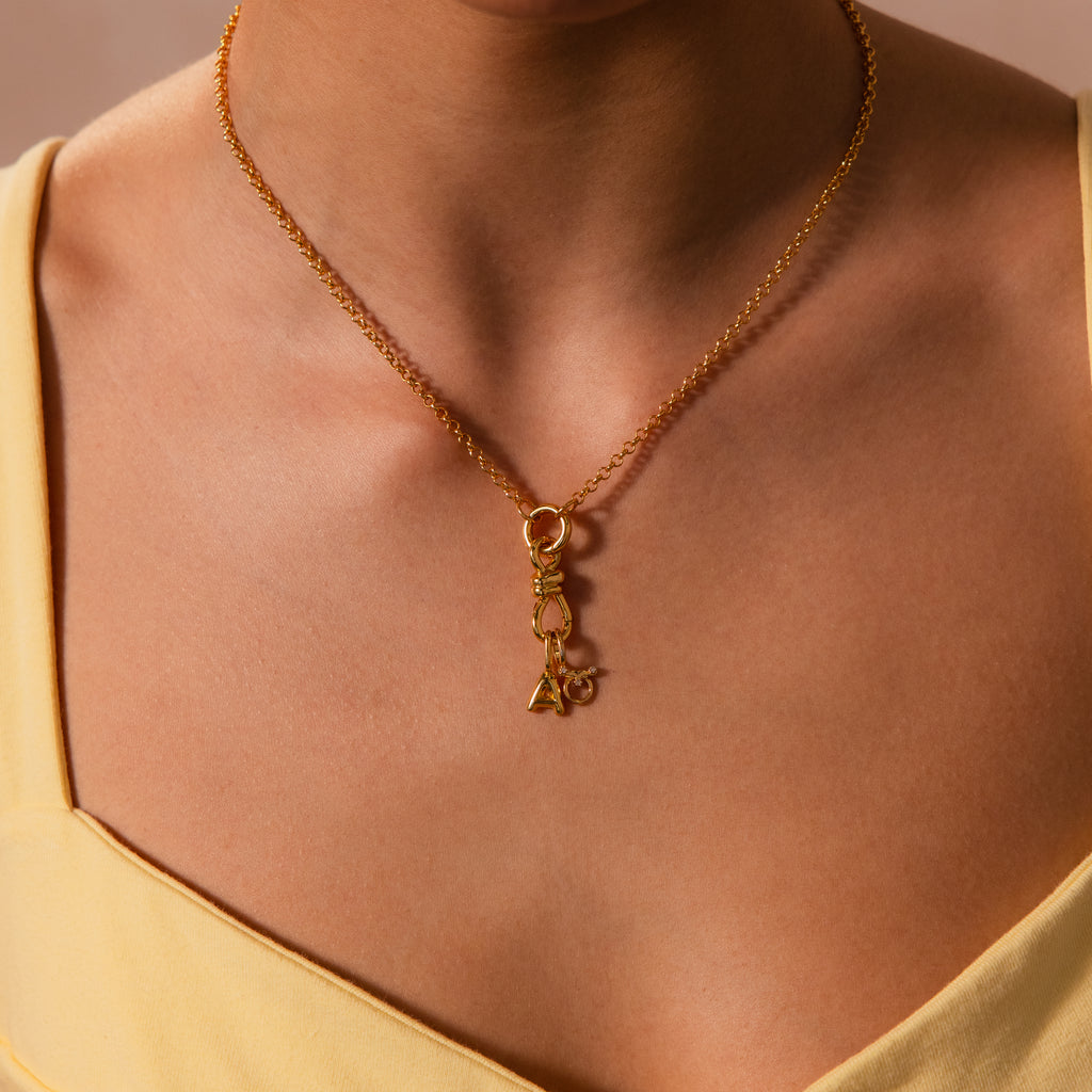 A woman showcases the Knot Charm Clasp gold necklace, its small geometric charms elegantly paired with a yellow V-neck top for a refined, modern style.