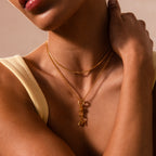 A woman in a yellow top gently touches her neck, showcasing two gold necklaces—one featuring the elegant Knot Charm Clasp pendant—perfect for highlighting exquisite jewelry styles.