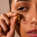 A person holding a Knot Charm Clasp near their face, showcasing detailed eye makeup and smooth skin—perfect for highlighting the clasp’s sophisticated design in any product description.