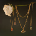 Birth Flower Charm Necklace pendants hang from a white rose stem against a dark background, creating an elegant product photo that highlights this unique jewelry piece.