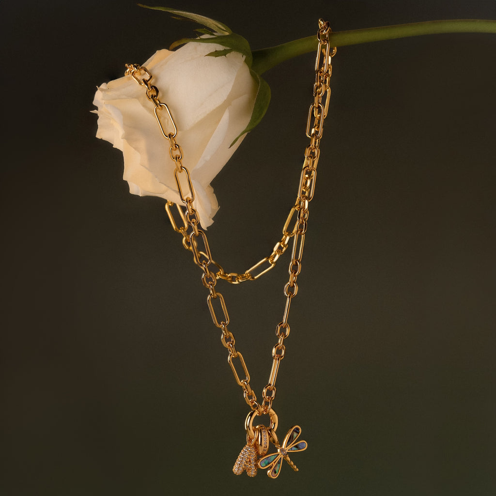 The Rolo Circle Figaro Necklace with charms is displayed draped over a white rose against a dark background.