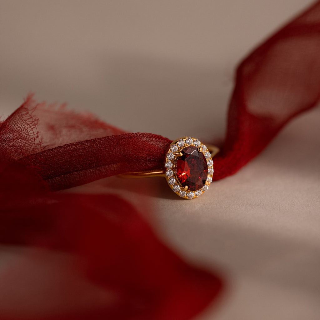 The Pave Garnet Ring features an oval red garnet, January's birthstone, accented by small diamonds and set against burgundy fabric for a stunning look.