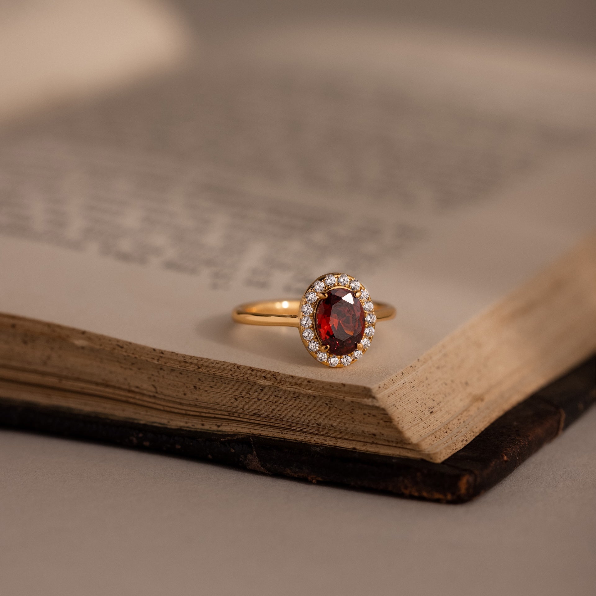 The Pave Garnet Ring, inspired by January’s birthstone and framed with sparkling diamonds, rests on the open pages of an old book.
