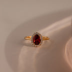 The Pave Garnet Ring showcases an oval red garnet, January's birthstone, accented by sparkling diamonds and set against a neutral background.