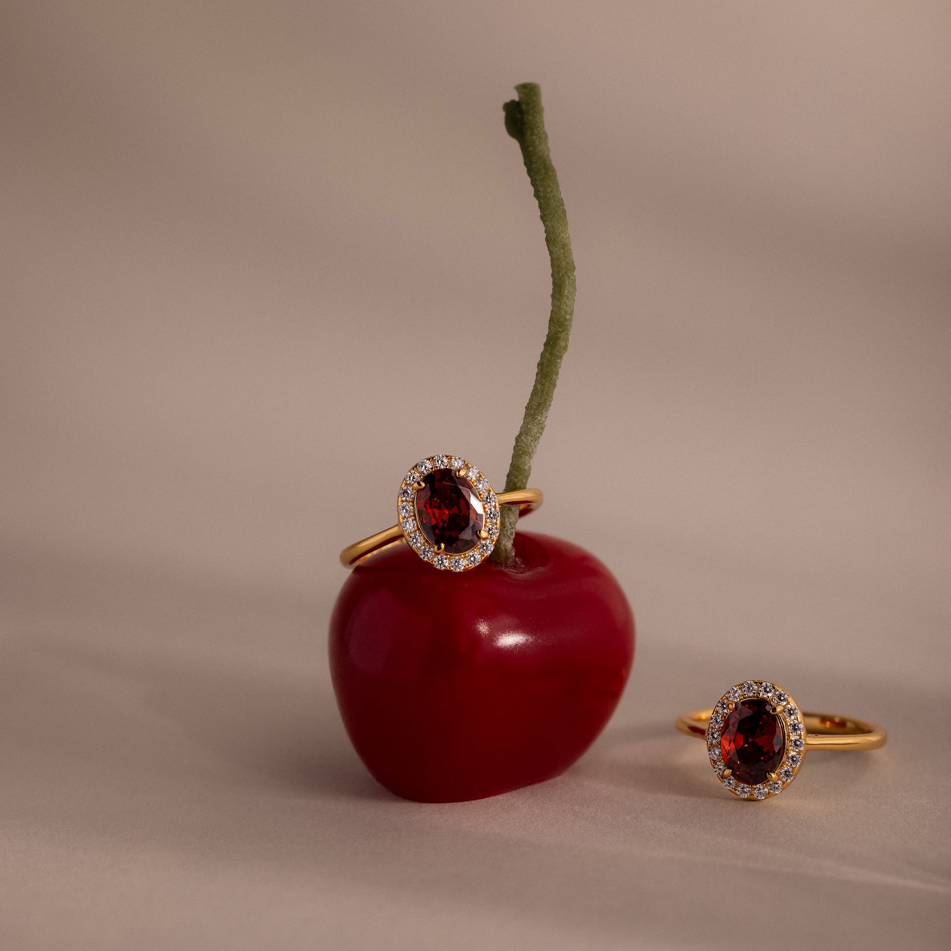 A Pave Garnet Ring, featuring vibrant red gemstones symbolic of January's birthstone, exudes elegance as it rests on a neutral surface beside a ripe cherry.
