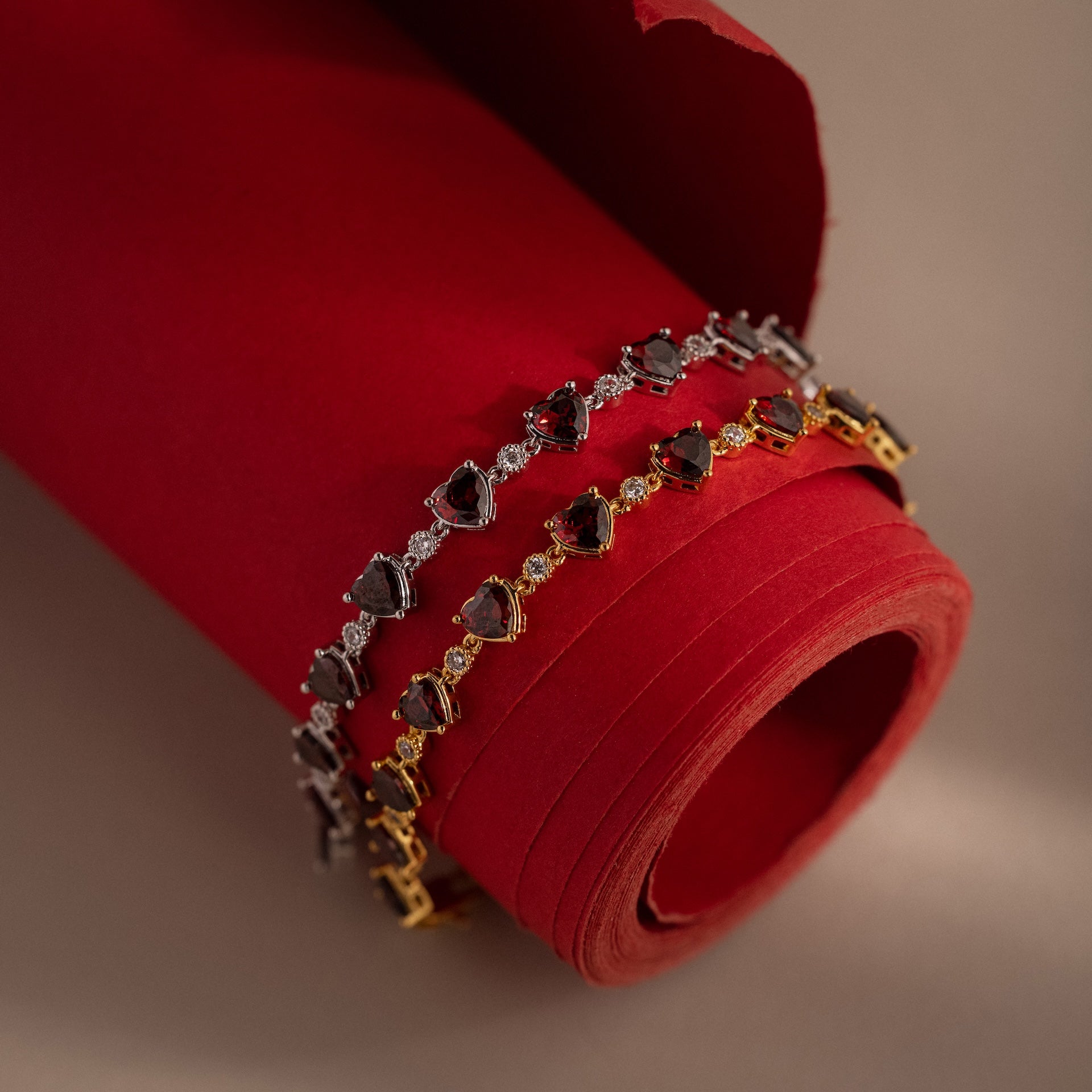 Two heart-shaped stone bracelets in silver and gold, shown on red fabric—wear alone or pair with our Garnet Heart Tennis Bracelet for a stunning statement.