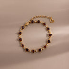 The Garnet Heart Tennis Bracelet in 18K Gold features red heart-shaped garnets, clear stones, an adjustable chain, and a heart charm—perfect as a standout statement bracelet.