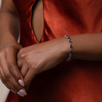Woman in a red satin dress wears the Garnet Heart Tennis Bracelet in Sterling Silver, featuring delicate heart-shaped garnets and white gemstones—a striking statement piece.