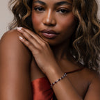 A woman in a red satin top showcases the Garnet Heart Tennis Bracelet in Sterling Silver, adorned with heart-shaped garnets, as her hand rests gently on her shoulder.