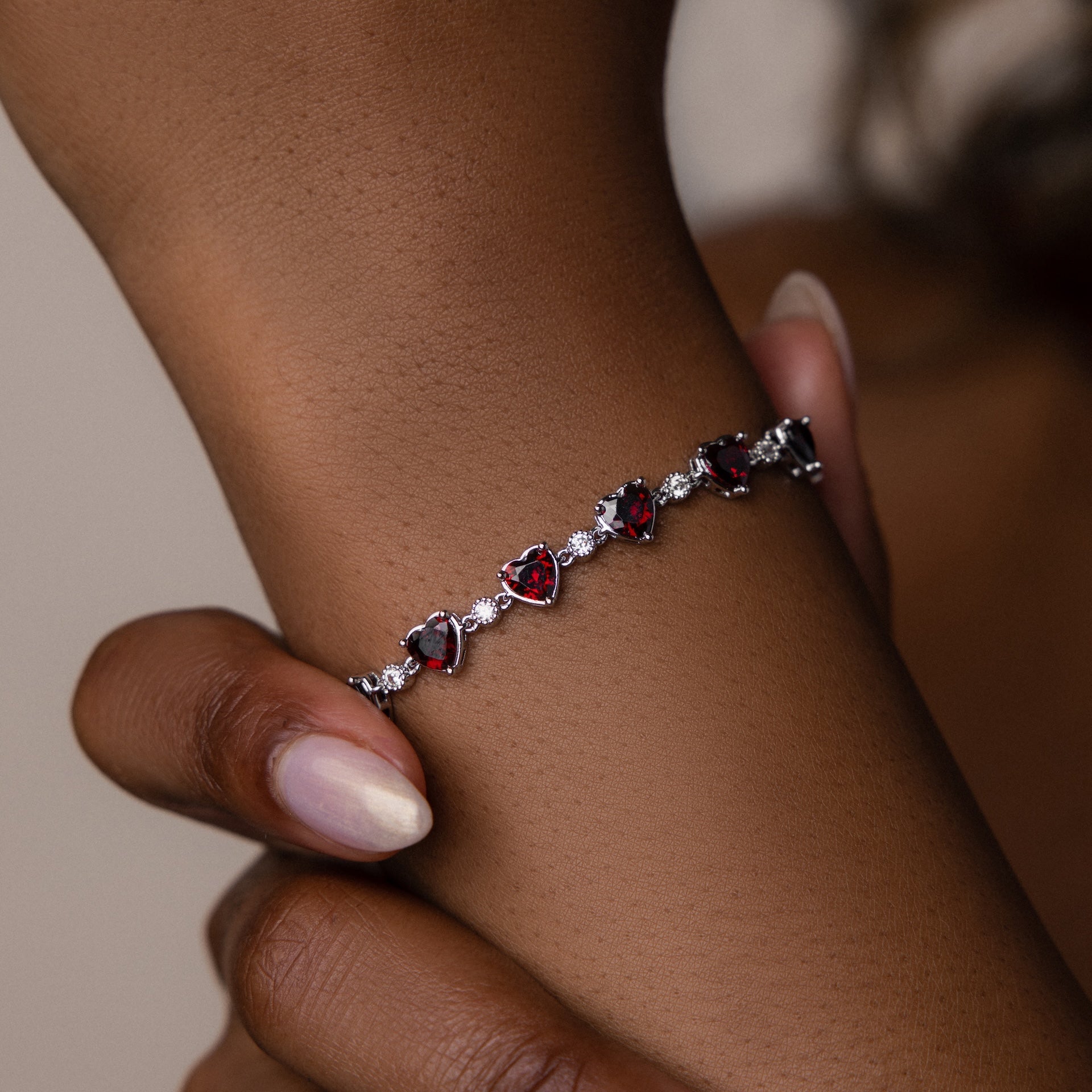 The Garnet Heart Tennis Bracelet in Sterling Silver, with its striking heart-shaped garnets, graces the wrist—a true statement piece.