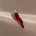 The Chili Pepper Charm in Sterling Silver features a red glass chili pendant with a silver loop, ideal for charm necklaces, shown on a neutral background with gentle lighting and shadows.