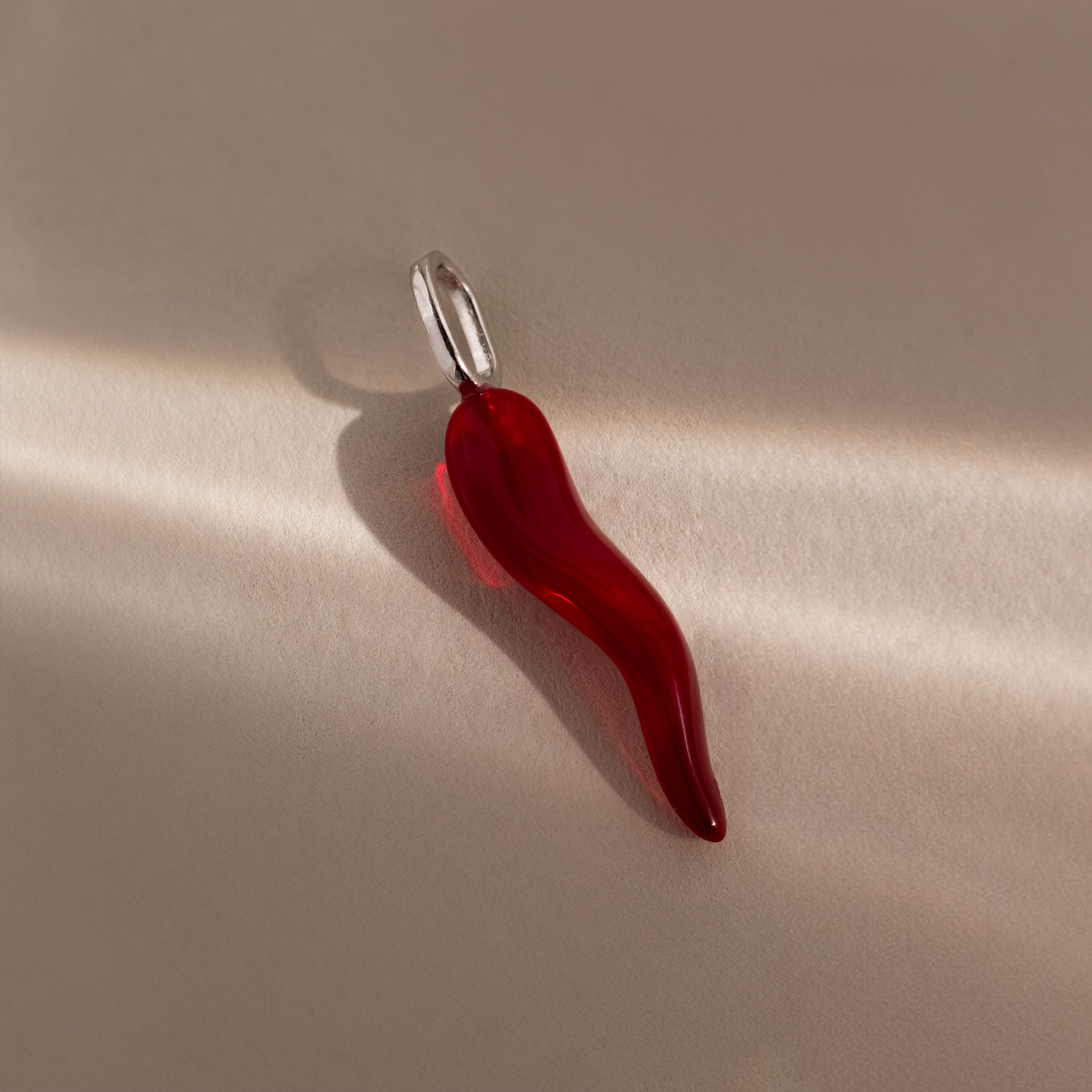 The Chili Pepper Charm in Sterling Silver features a red glass chili pendant with a silver loop, ideal for charm necklaces, shown on a neutral background with gentle lighting and shadows.