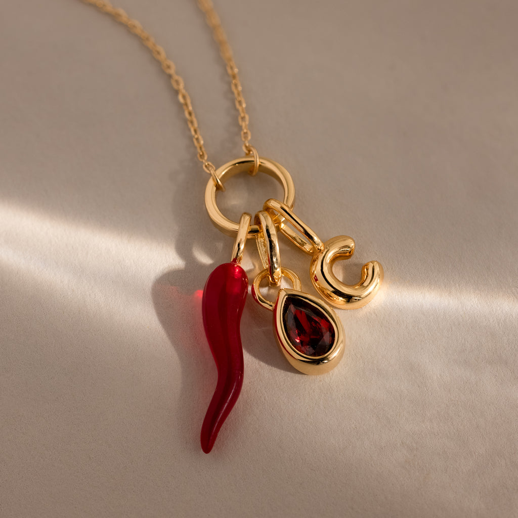 The Chili Pepper Charm necklace features a gold chain with three unique charms: a vibrant chili pepper, a sparkling teardrop gem, and a gold letter C for personalized style.