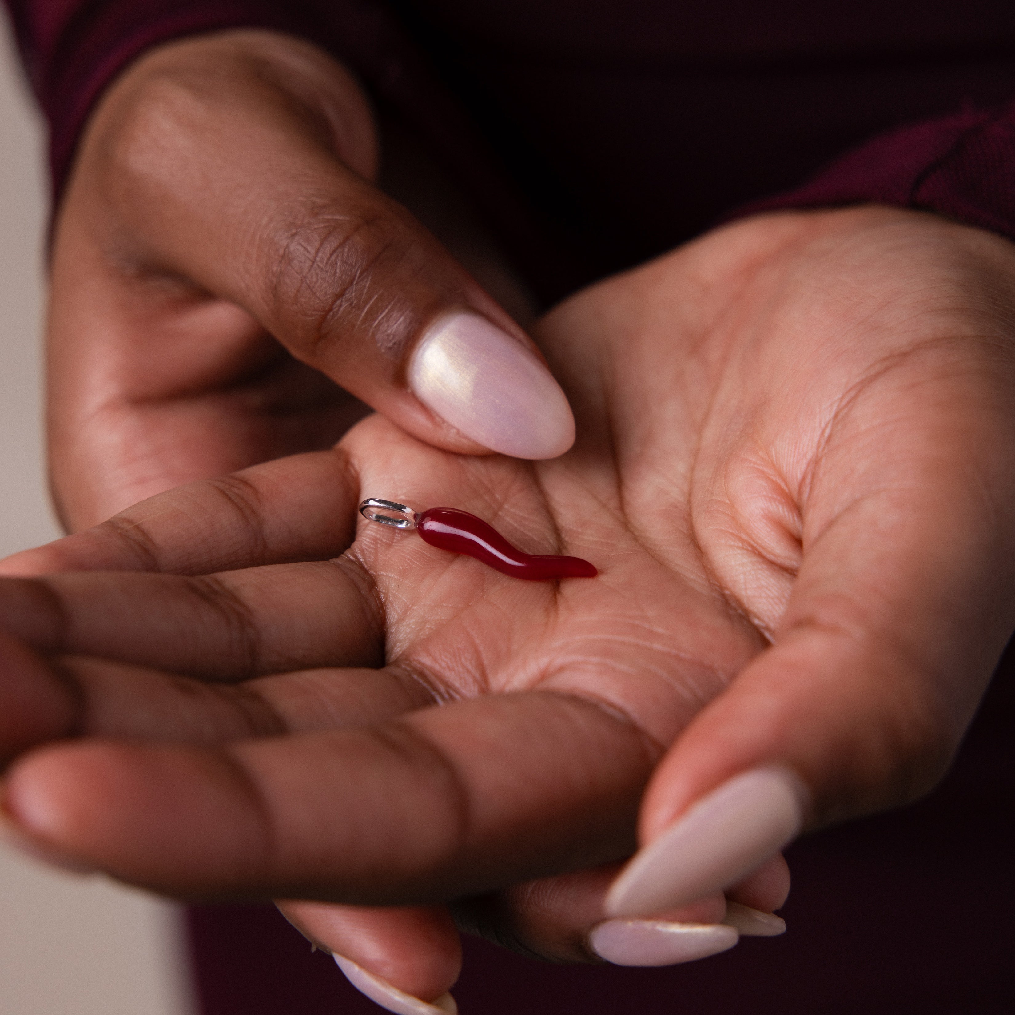 A hand with manicured nails displays the Chili Pepper Charm, showcasing this distinctive jewelry piece.