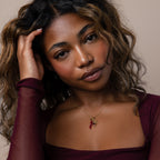 A woman with wavy hair in a burgundy top showcases the Chili Pepper Charm gold necklace, posing with her hand near her face.