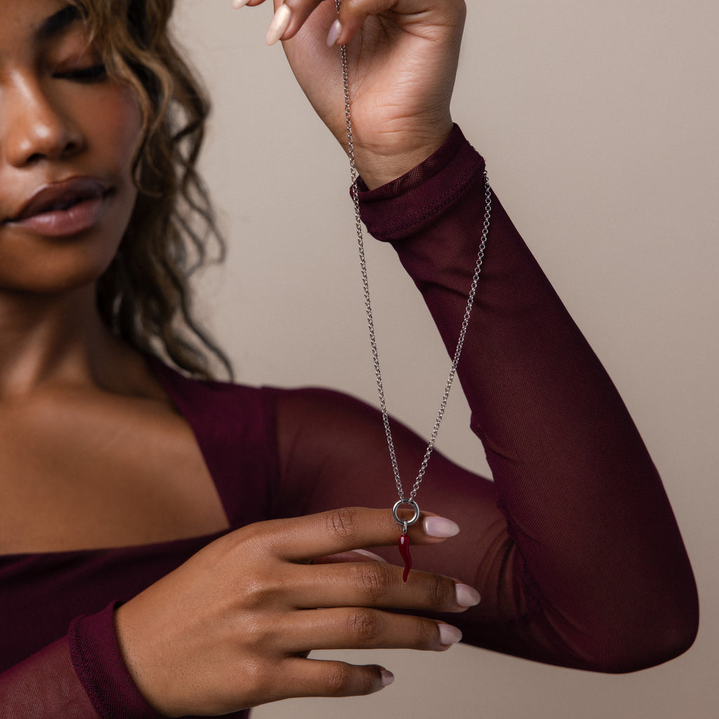 A woman in a burgundy top holds a Chili Pepper Charm in Sterling Silver necklace with a red pendant against a neutral background.