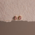 The Rhombus Pink Tourmaline Flatback Studs add modern glamour with their small pink stones and gold settings on a textured beige surface.