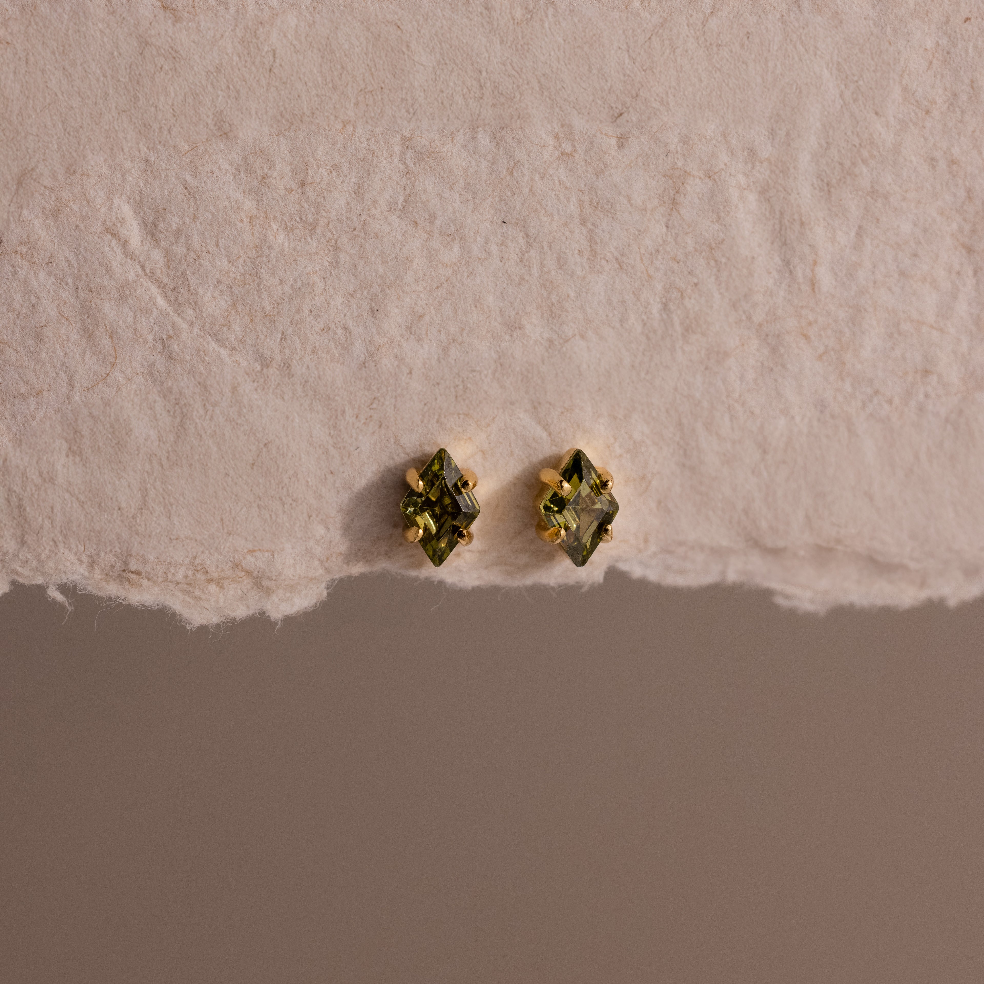 Rhombus Peridot Flatback Studs with gold settings shown on a textured off-white surface—ideal for adding a pop of modern green glamour.