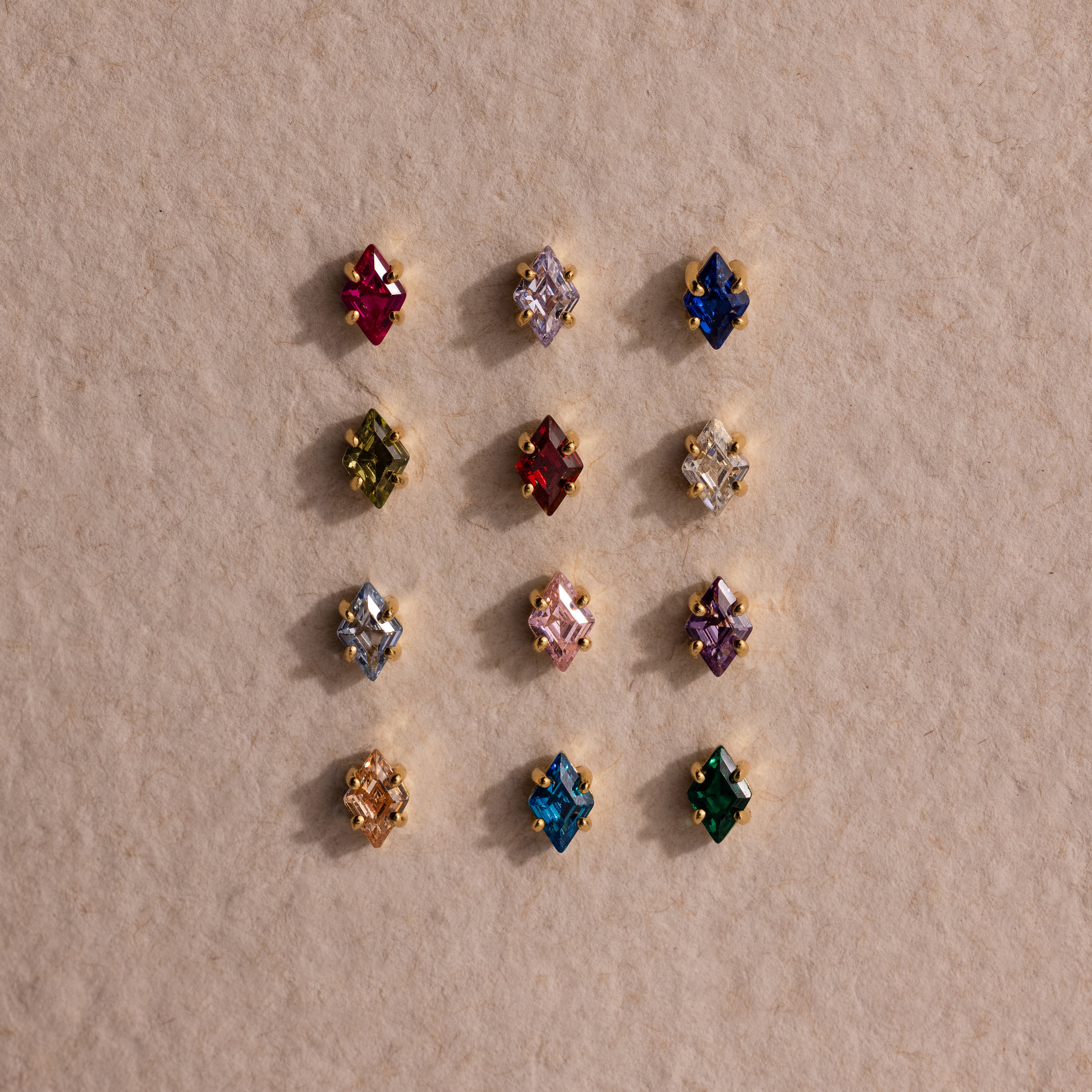 Twelve vibrant Rhombus Pink Tourmaline Flatback Studs are arranged in a grid on a textured beige surface, bringing modern glamour and a pop of color to any jewelry collection.