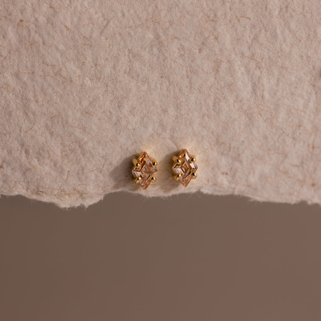 Rhombus Topaz Flatback Studs—small earrings blending gold and diamond accents with modern glamour, shown on a textured beige background.