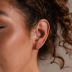 A woman's ear adorned with Rhombus Topaz Flatback Studs sparkles with modern glamour, while her curly hair softly frames her face.