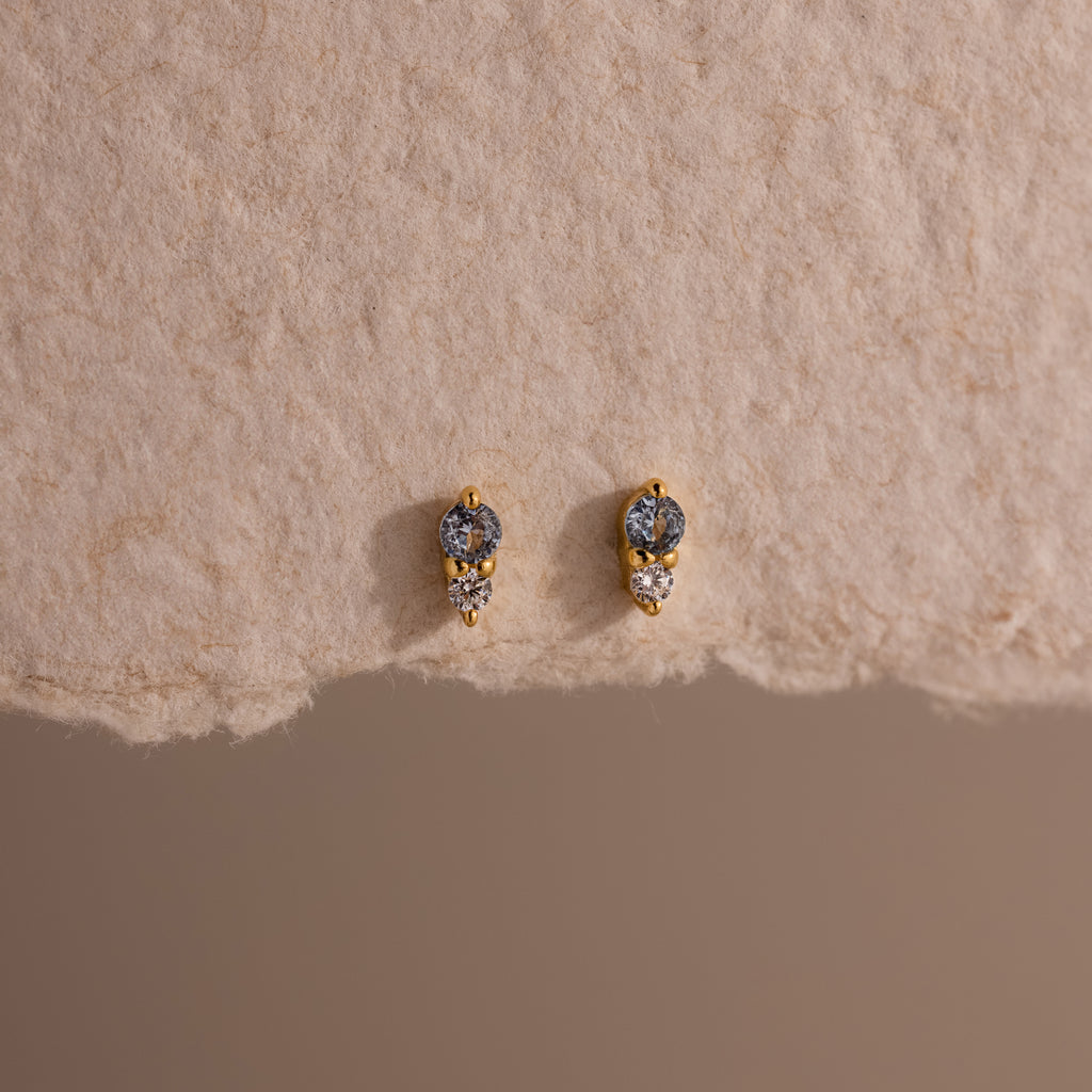 Tiny Duo Aquamarine Flatback Studs with blue and clear stones, a subtle diamond accent, displayed on textured beige paper.