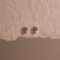 Tiny Duo Aquamarine Flatback Studs with blue and clear stones, a subtle diamond accent, displayed on textured beige paper.