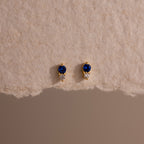 Tiny Duo Sapphire Flatback Studs—gold earrings with blue and clear stones, diamond accents, and shown on textured beige paper—perfect for your ear stack.