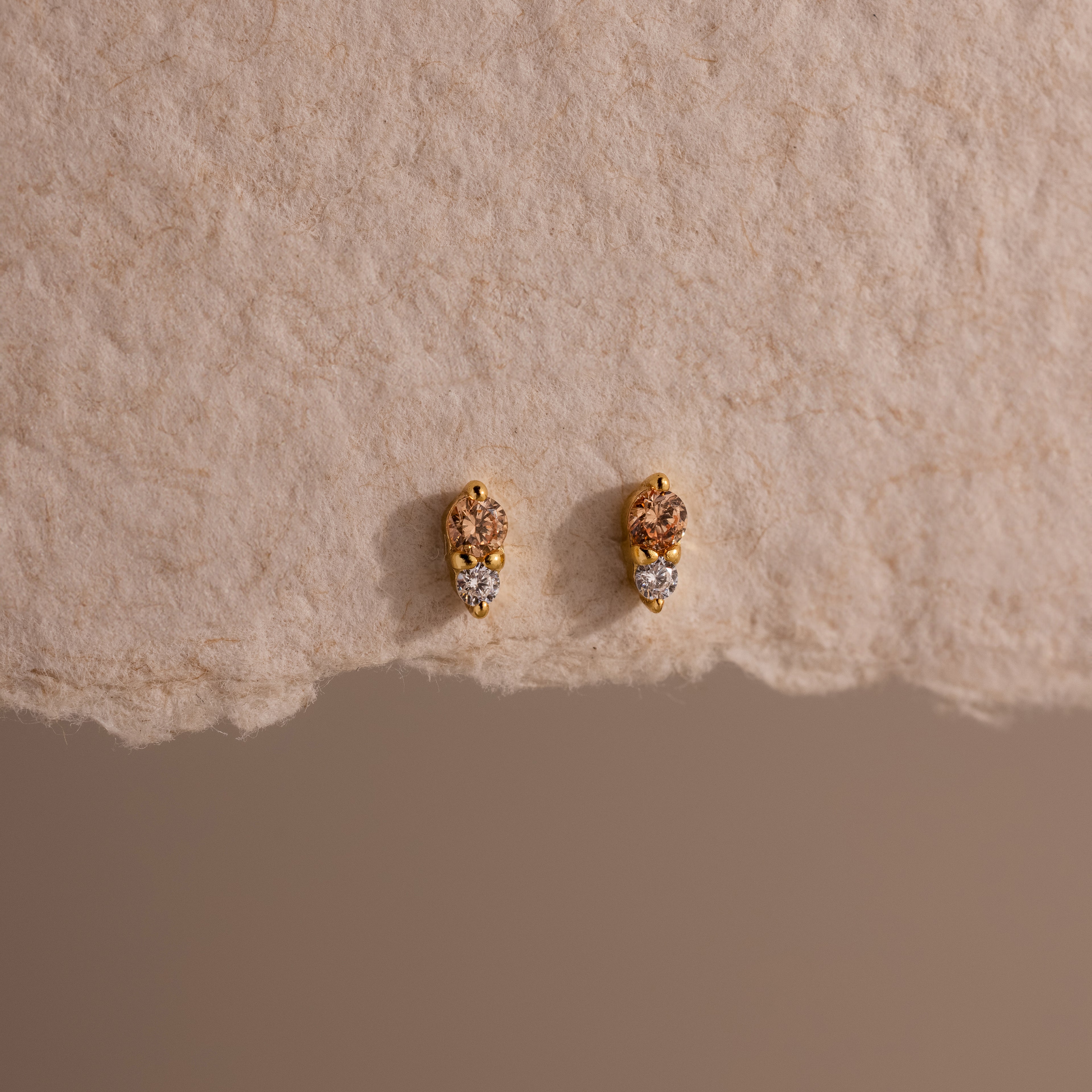 Tiny Duo Topaz Flatback Studs with a delicate diamond accent, displayed on a textured beige paper background.