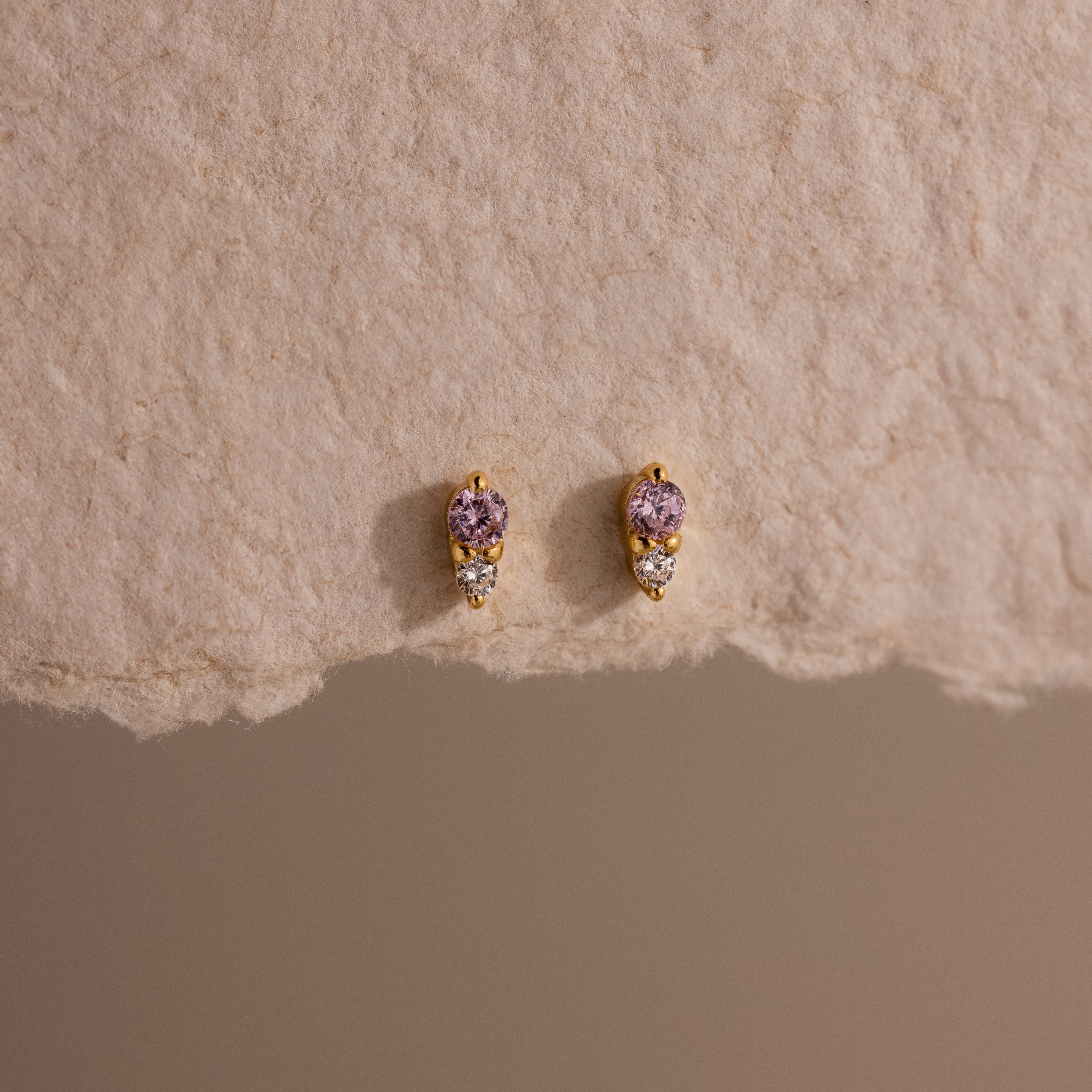 Tiny Duo Alexandrite Flatback Studs featuring purple birthstones and diamond accents, displayed on textured beige paper—perfect for your ear stack.