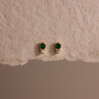 Tiny Duo Emerald Flatback Studs with green and clear stones, perfect for ear stacking, displayed on a textured beige surface.