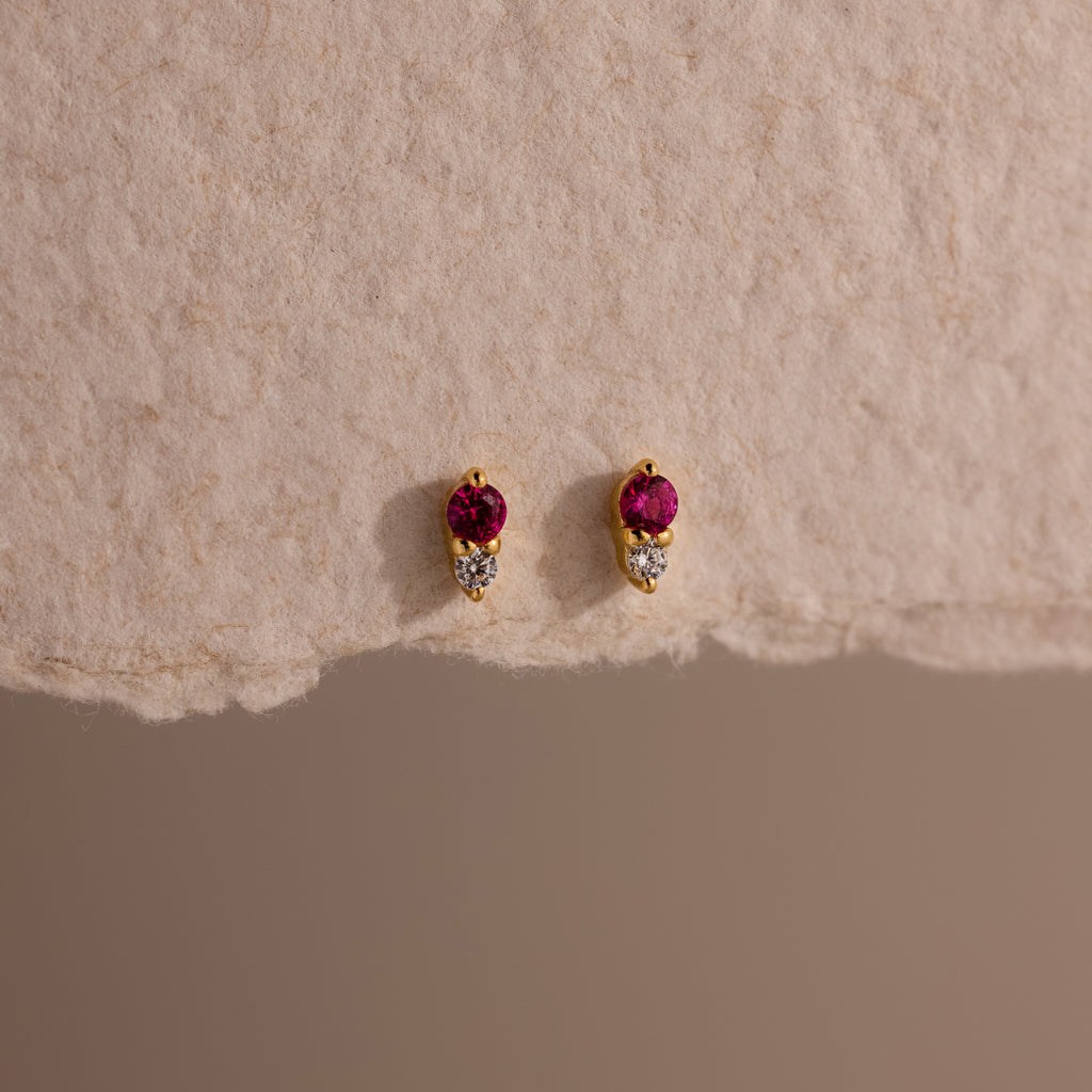 Tiny Duo Ruby Flatback Studs featuring small red and clear stones, displayed on textured beige paper.